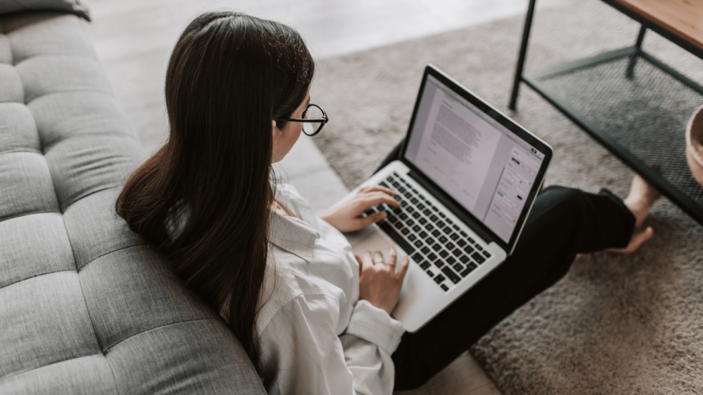 A smiling person with glasses sitting at a desk with a laptop