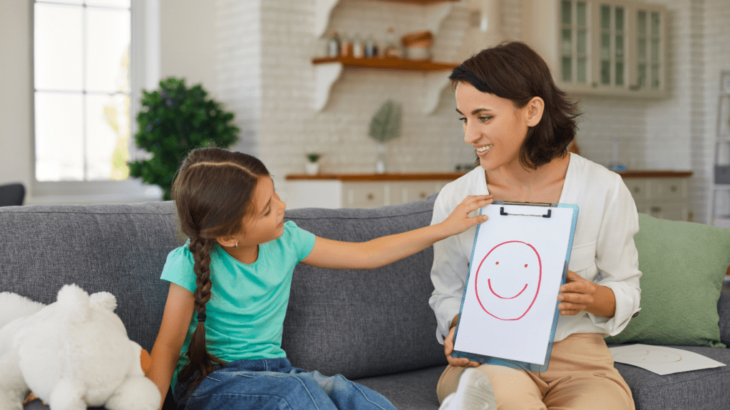 A person and a child sitting on a couch with a smiley face drawn on a piece of paper