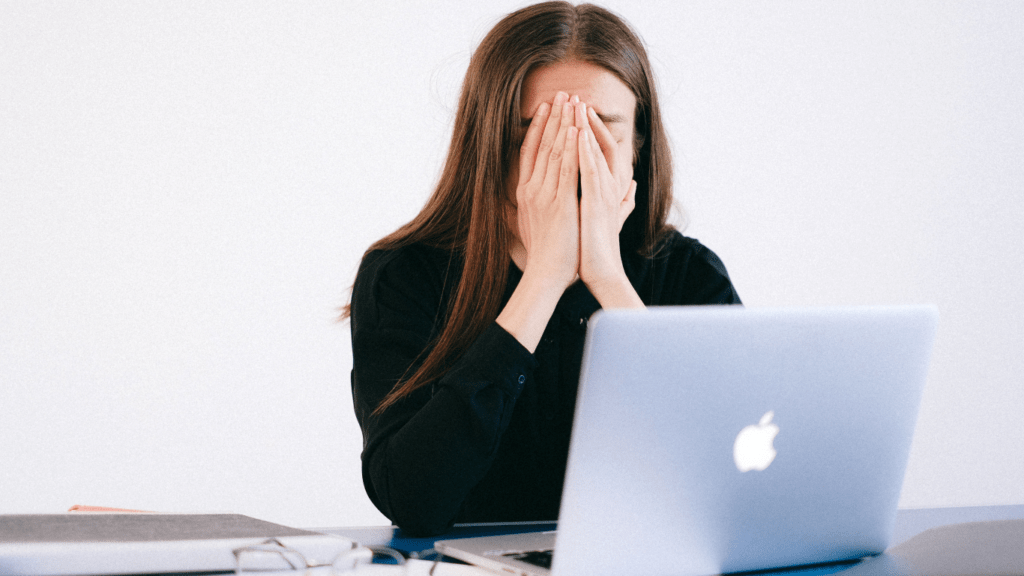 a person sitting in front of a laptop with their head in their hands