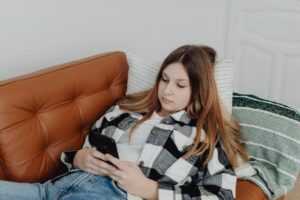 A teenage girl looking at her phone on the couch.