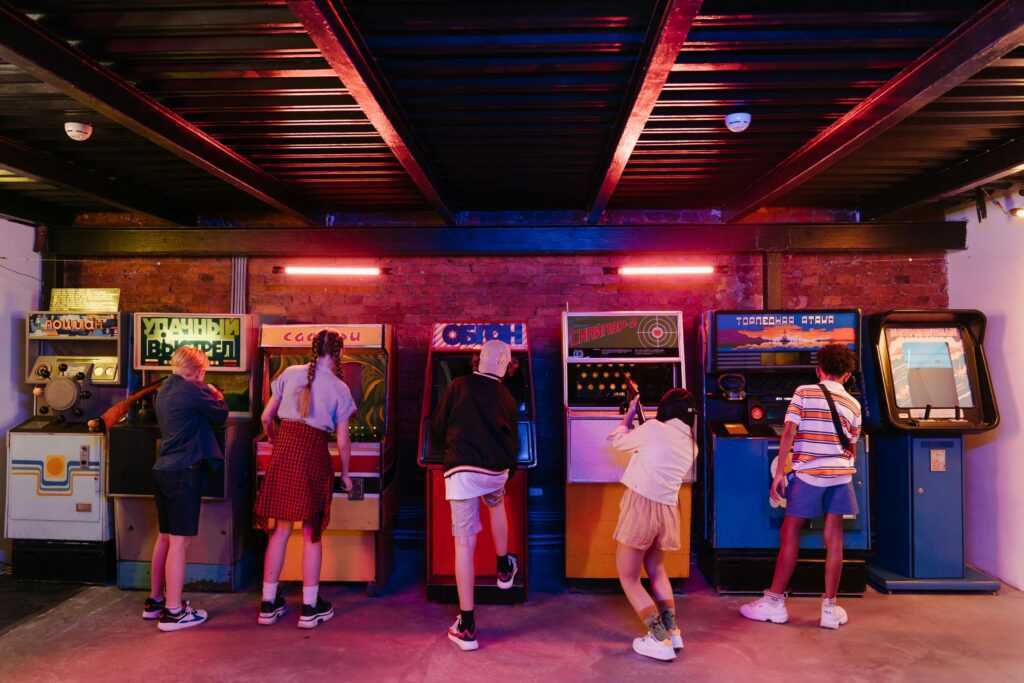 Group of teenagers playing various retro arcade games, enjoying a nostalgic gaming experience.