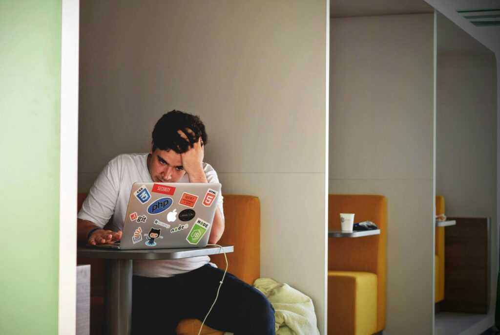 A stressed man looking at his laptop with stickers, in a cafe. 