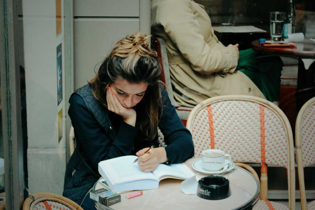 A woman studying from a book in a cafe, looking bored.
